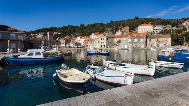 A harbor with boats docked, buildings with red roofs, and a hillside in the background. - Apartment Mali Skoj - Two-Bedroom Apartment with Sea View (Sudurad)