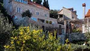 A stone building with multiple windows and a red-tiled roof, surrounded by greenery. - Apartment Mali Skoj - Two-Bedroom Apartment with Sea View (Sudurad)