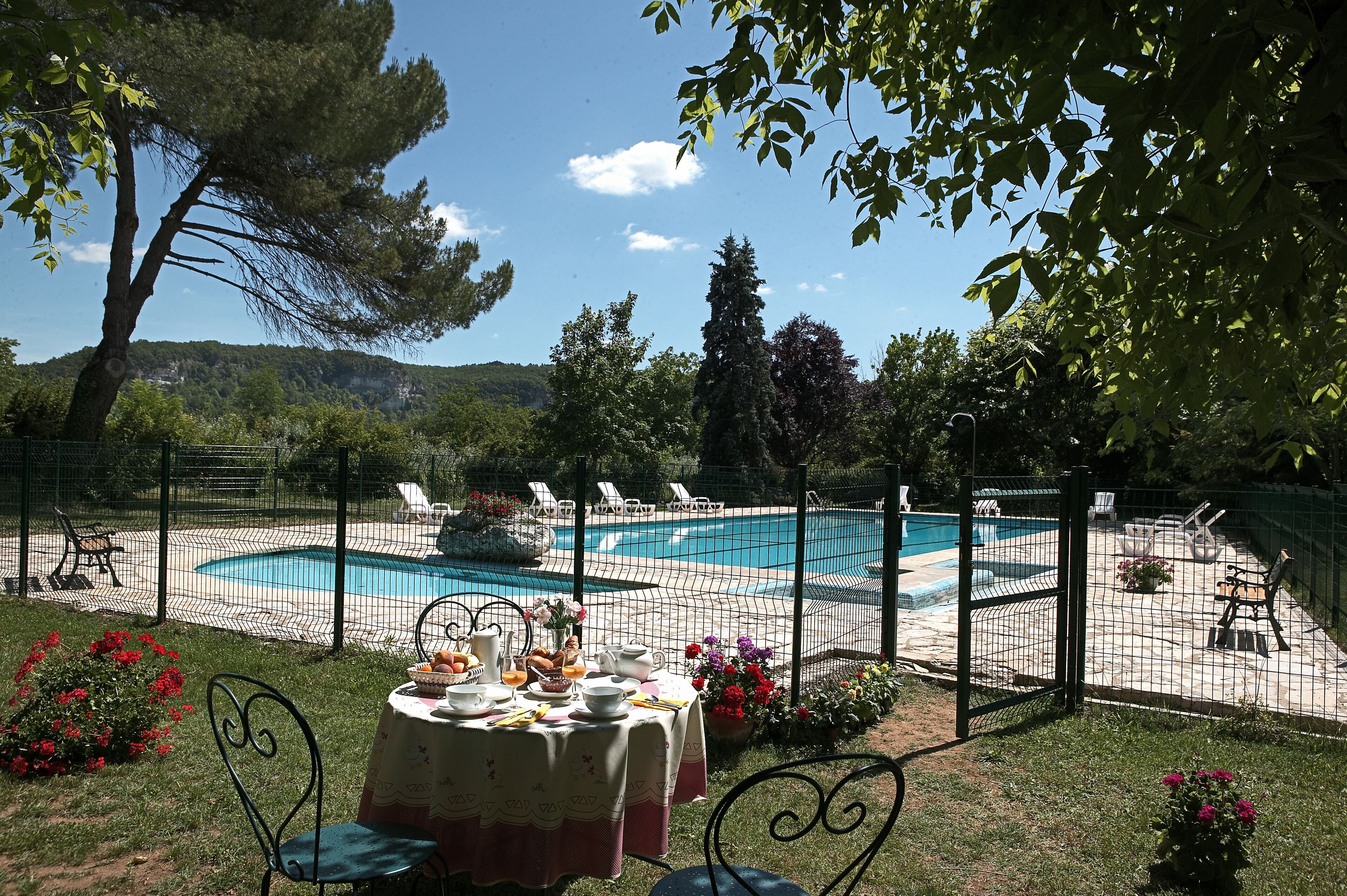 Un espace aménagé au bord de la piscine, avec une table dressée pour le petit-déjeuner, entouré d’une clôture et donnant sur une piscine.
