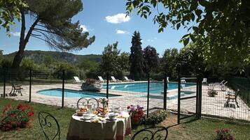 Un espace aménagé au bord de la piscine, avec une table dressée pour le petit-déjeuner, entouré d’une clôture et donnant sur une piscine.