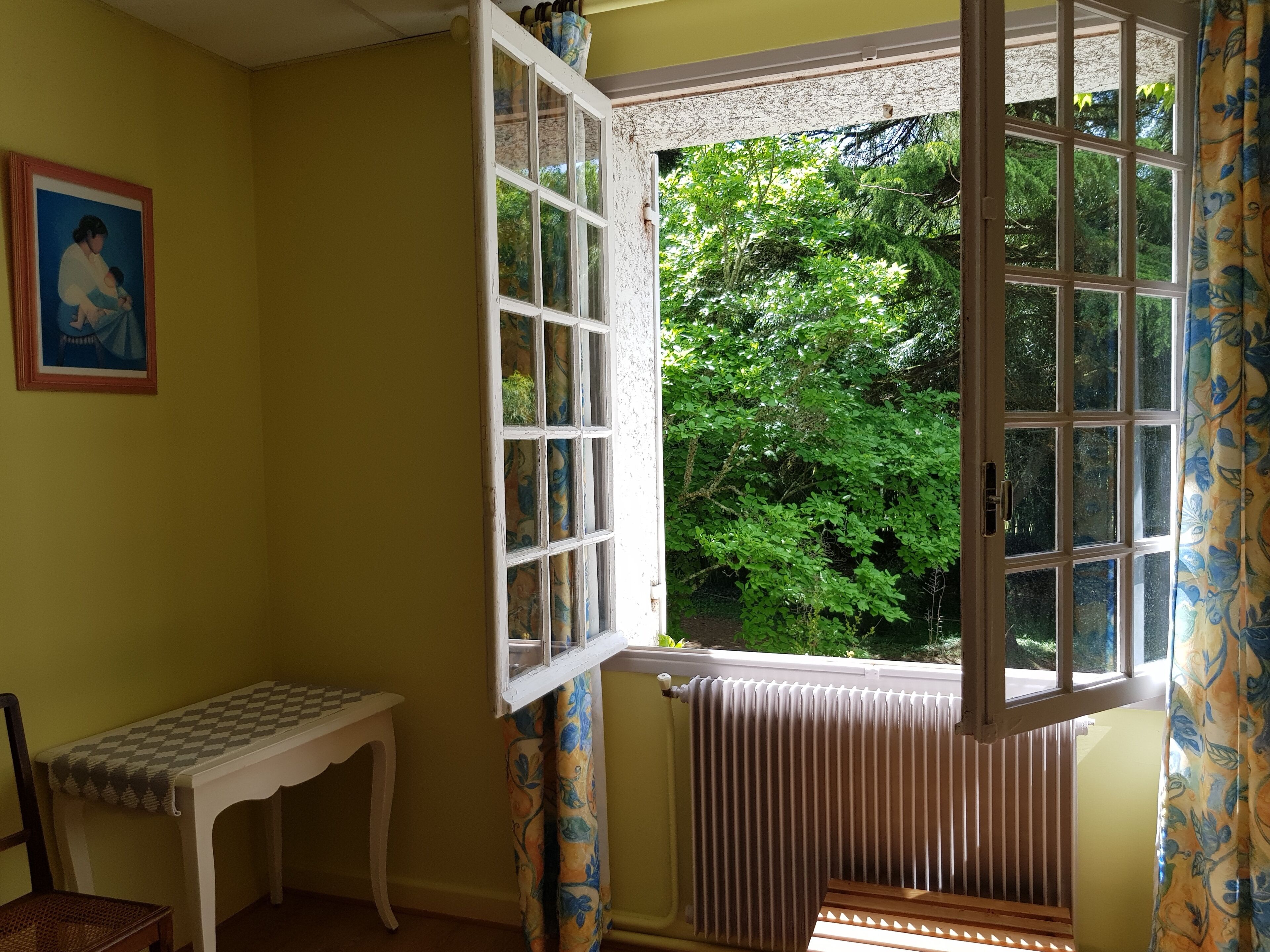 Une pièce avec un bow-window, un radiateur, un banc et un tableau encadré au mur.