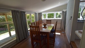 Un comedor con mesa y sillas de madera, ventanas grandes con cortinas y vista a áreas verdes.