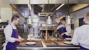 A professional kitchen with stainless steel appliances, chefs in aprons, and a buffet setup. - Maison Tiegezh (Guer)
