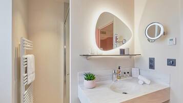 Un baño moderno con un espejo grande, un lavabo con una planta en maceta y un perchero para toallas.