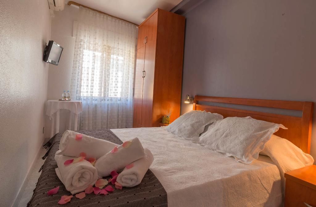 A hotel room with a bed, a wooden wardrobe, a television mounted on the wall, and a window with curtains.