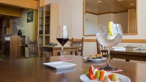 A dining area with a wooden table, two wine glasses, a plate with fruit skewers, and a small white plate with a dessert. - Hostal Arribes Del Duero (Fermoselle)