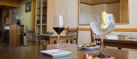 Un comedor con una mesa de madera, dos copas de vino, un plato con brochetas de fruta y un plato pequeño blanco con un postre.