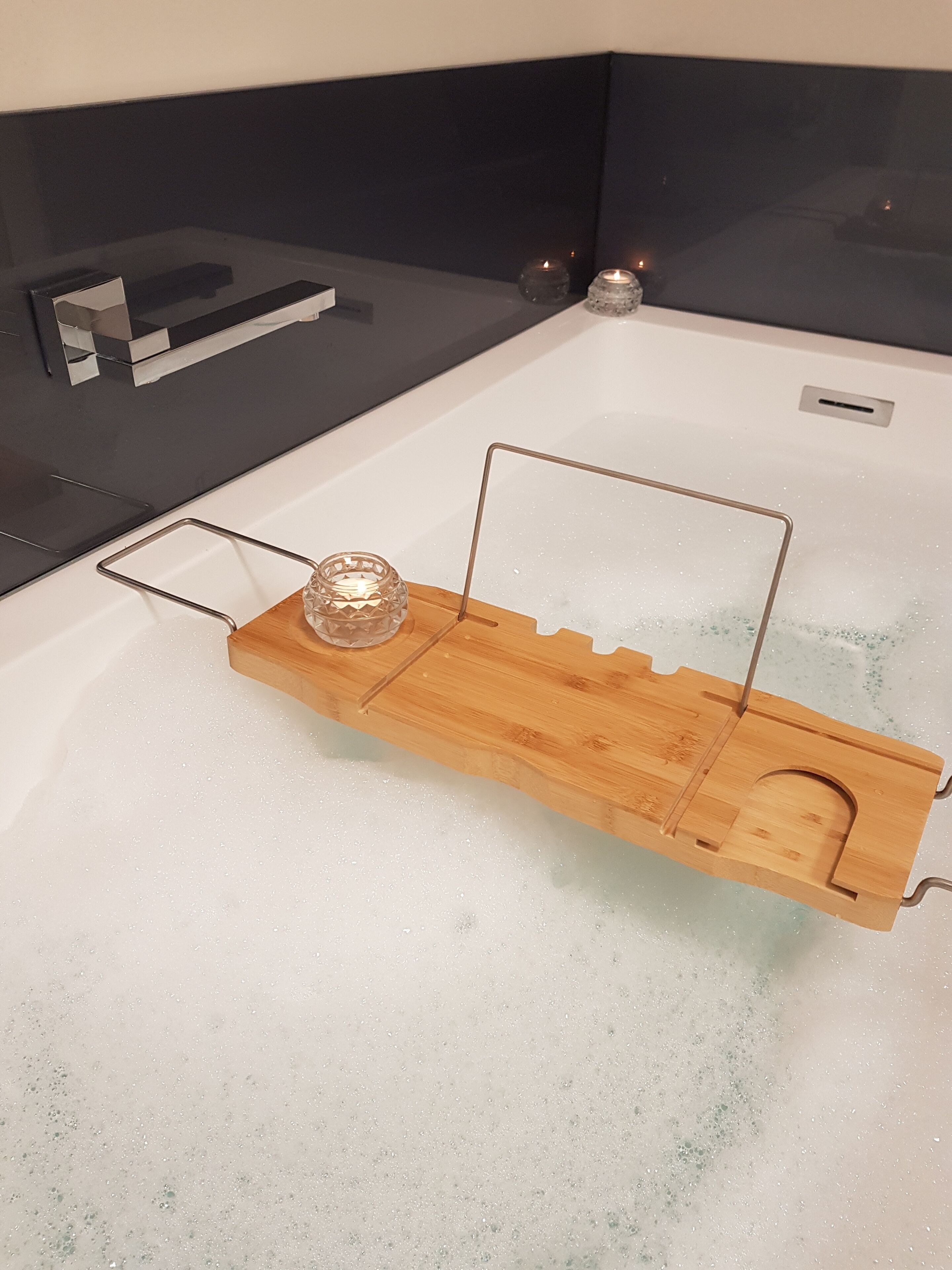 Eine Badewanne mit einem Holztablett, das eine Kerze und einen Metallrahmen trägt.