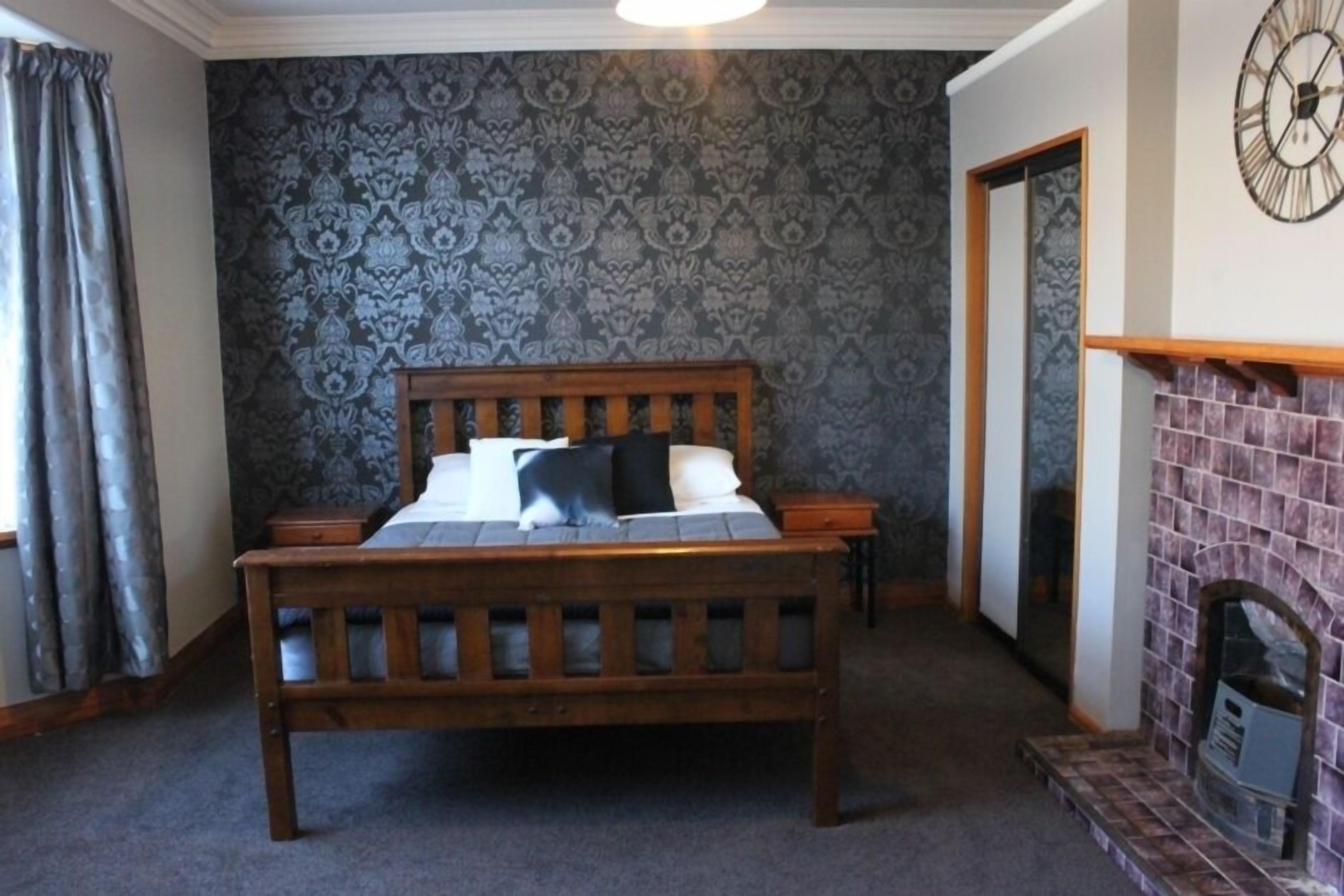 Une chambre à coucher avec un lit en bois, un papier peint à motifs, une cheminée et un miroir au mur.