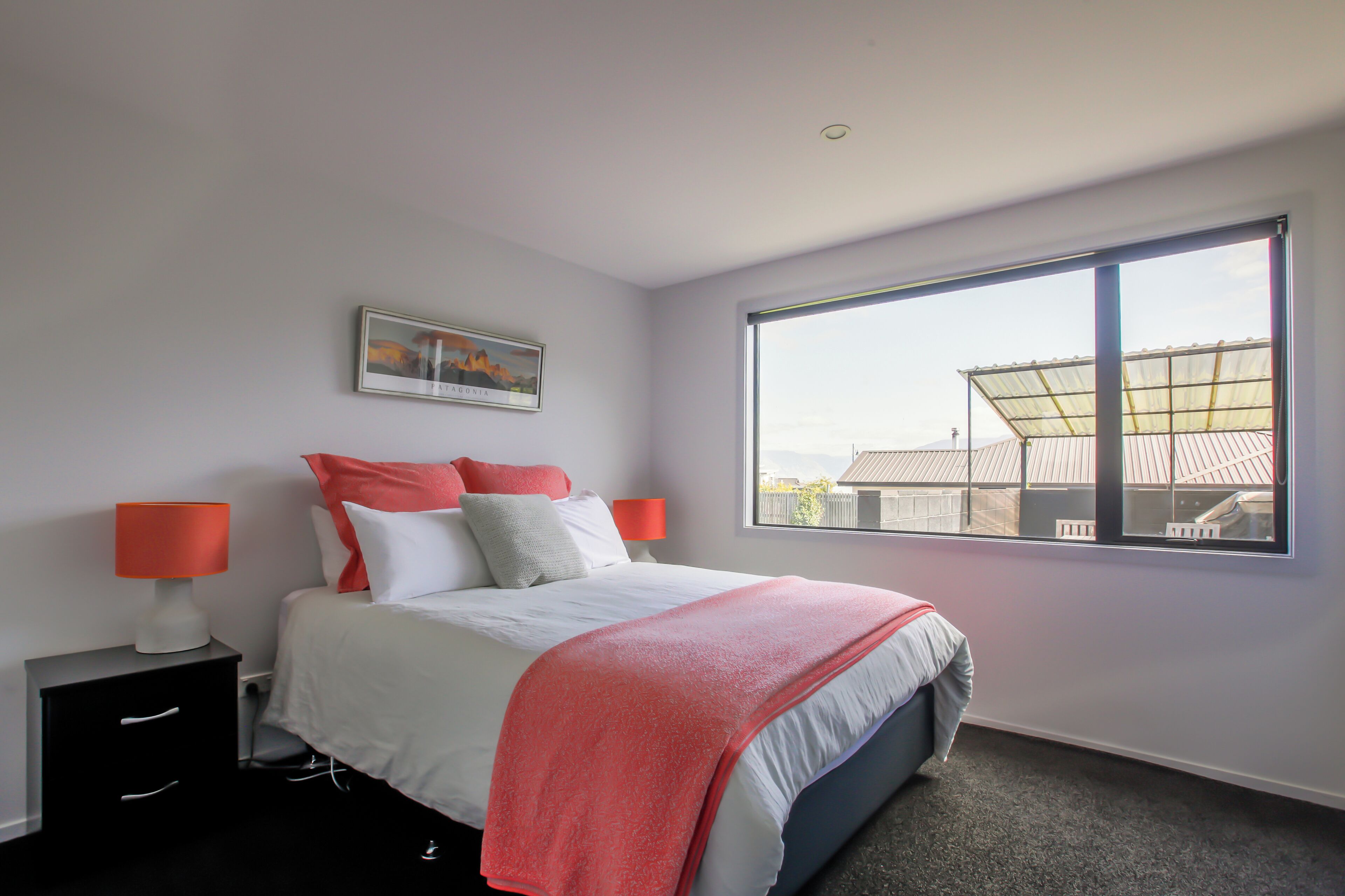 A bedroom with a bed, nightstands, a window, and a view of buildings.