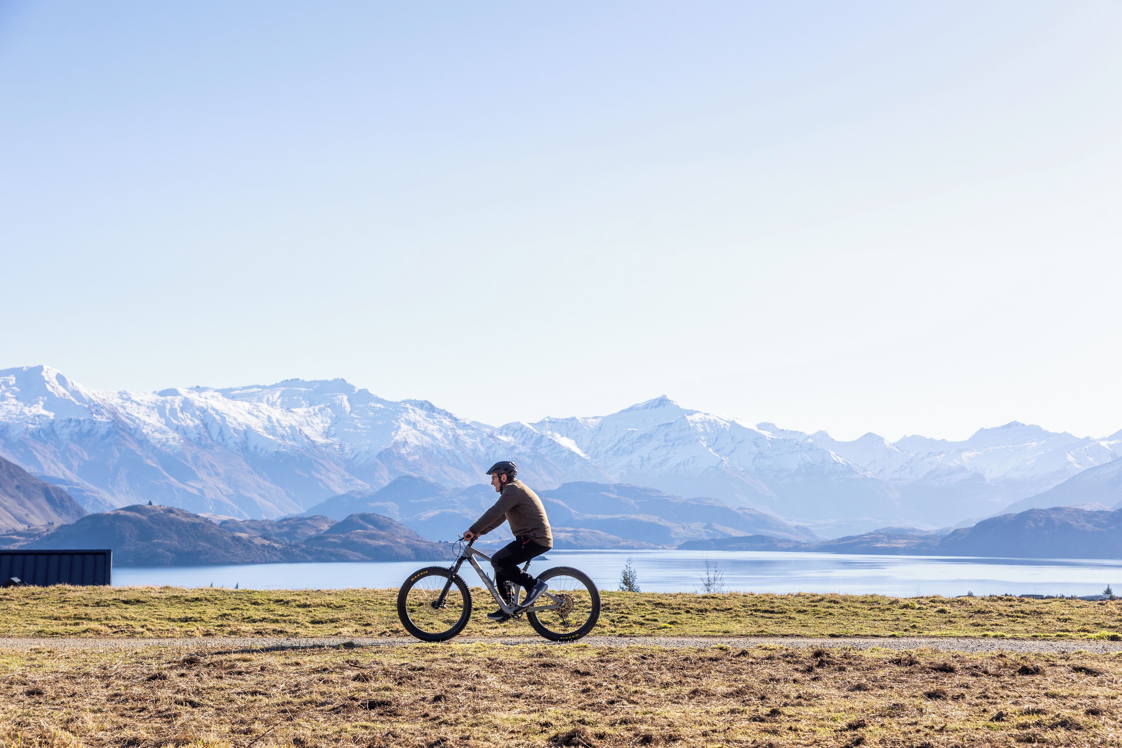 A person riding a mountain bike on a path with a lake and mountains in the background.