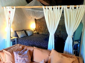 A bedroom with a bed, two bedside tables, a nightstand, a lamp, a stone wall, and a canopy bed with curtains. - Finca La Principal (Brena Alta)