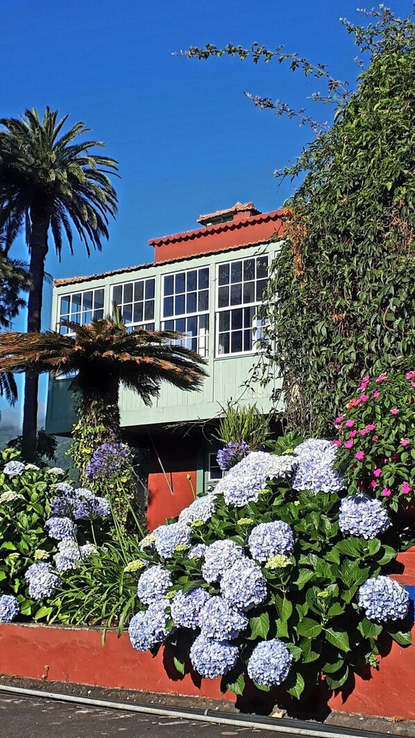 A building with a red roof and white windows, surrounded by lush greenery and hydrangea flowers. - Finca La Principal (Brena Alta)