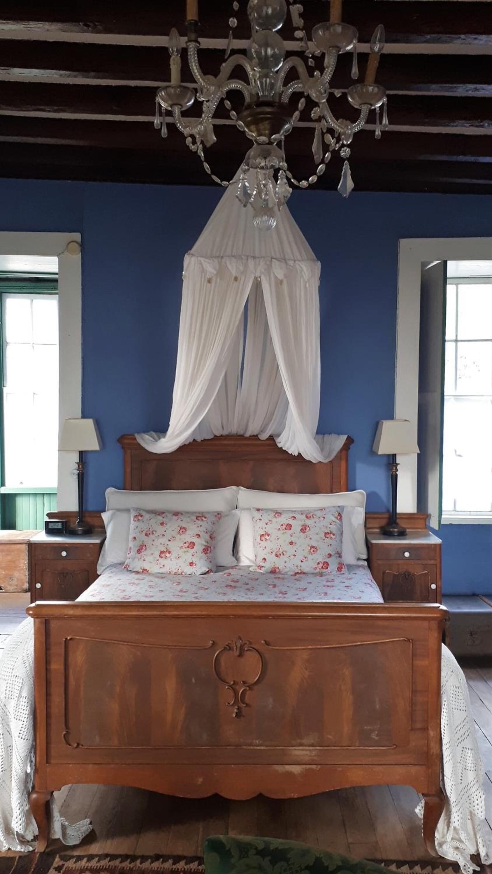 Un dormitorio con cama de madera, dos lámparas de noche, dosel blanco y ropa de cama floral, además de una araña.
