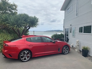 Une voiture de sport rouge est garée devant une maison qui offre une vue sur la mer.