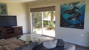 Una sala de estar con un sofá, una mesa de centro de vidrio, un televisor de pantalla plana sobre un mueble de madera y un cuadro grande de delfines en la pared.