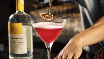 Un barman prépare un cocktail à l’aide d’une bouteille de gin et d’un verre à martini, le tout sur le comptoir du bar.