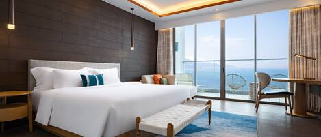 A modern hotel room with a large bed, a small seating area, and a balcony with a view of the sea.