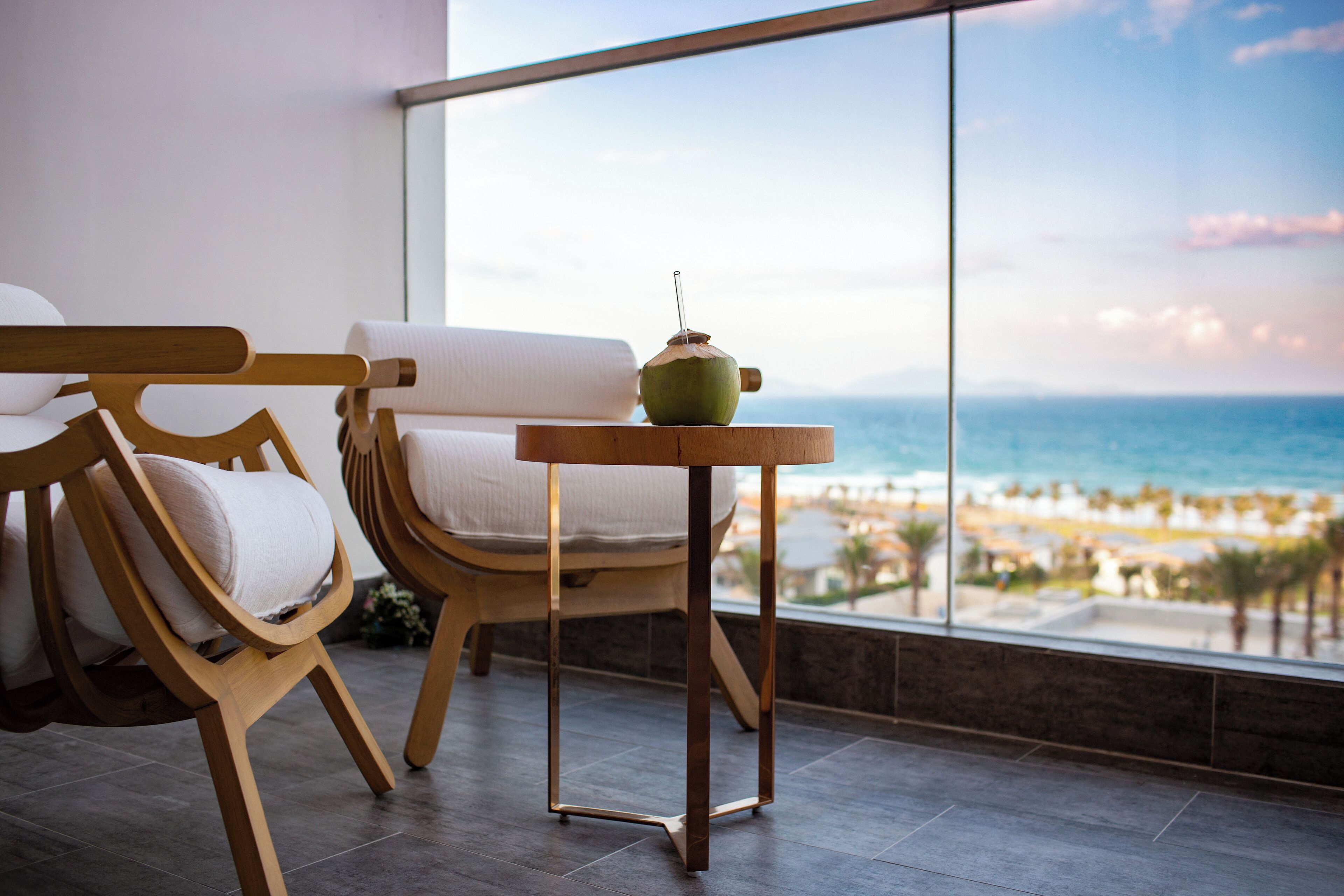 A modern room with a large window overlooking a beach, featuring wooden chairs and a small table.