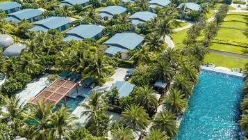 A resort with multiple blue-roofed villas surrounded by palm trees and a large swimming pool.
