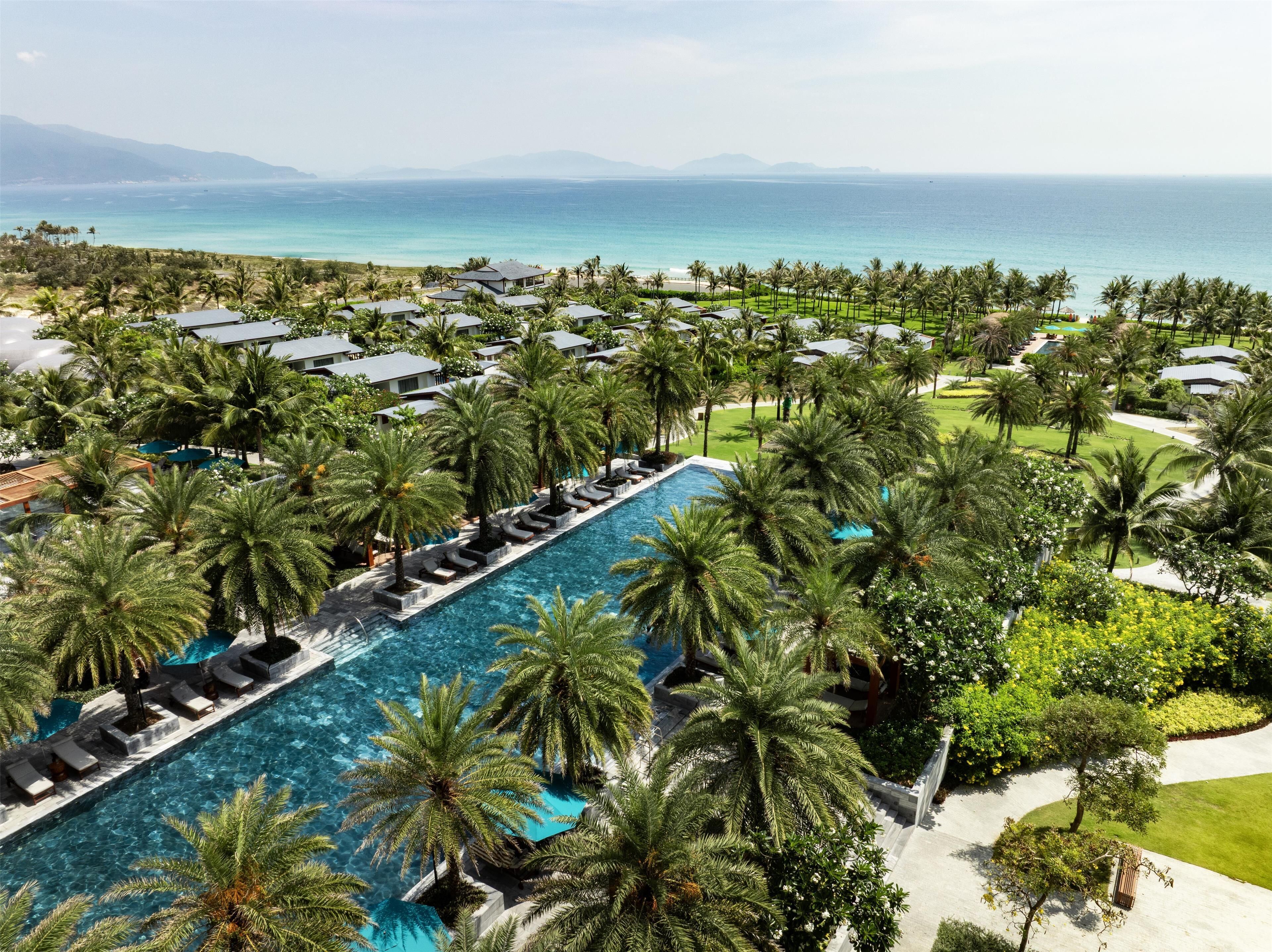 Un resort con una piscina larga rodeada de palmeras y vista al océano.