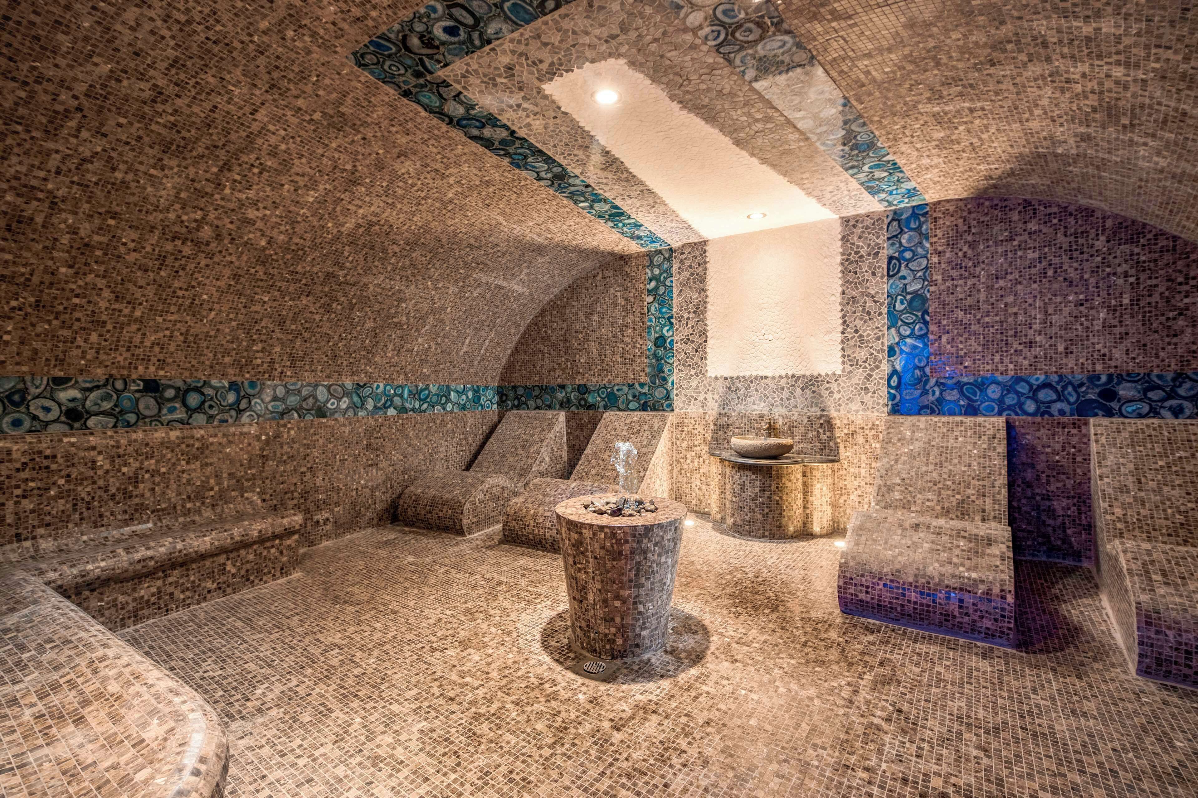 A room with mosaic tile walls and floor, a central pillar, and a small fountain.
