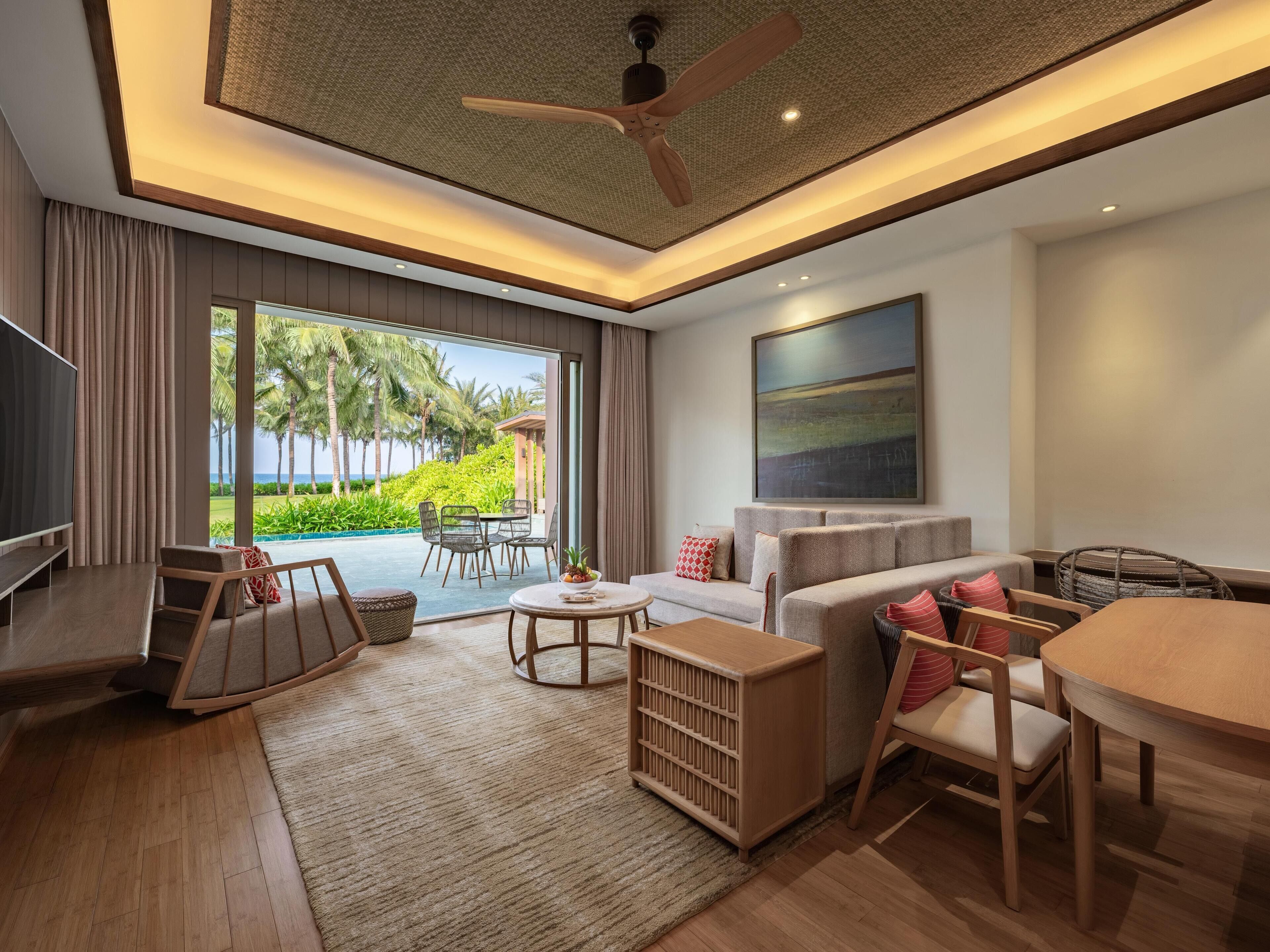 Una sala moderna con televisor, sofá, mesa de comedor y vista a un paisaje tropical.