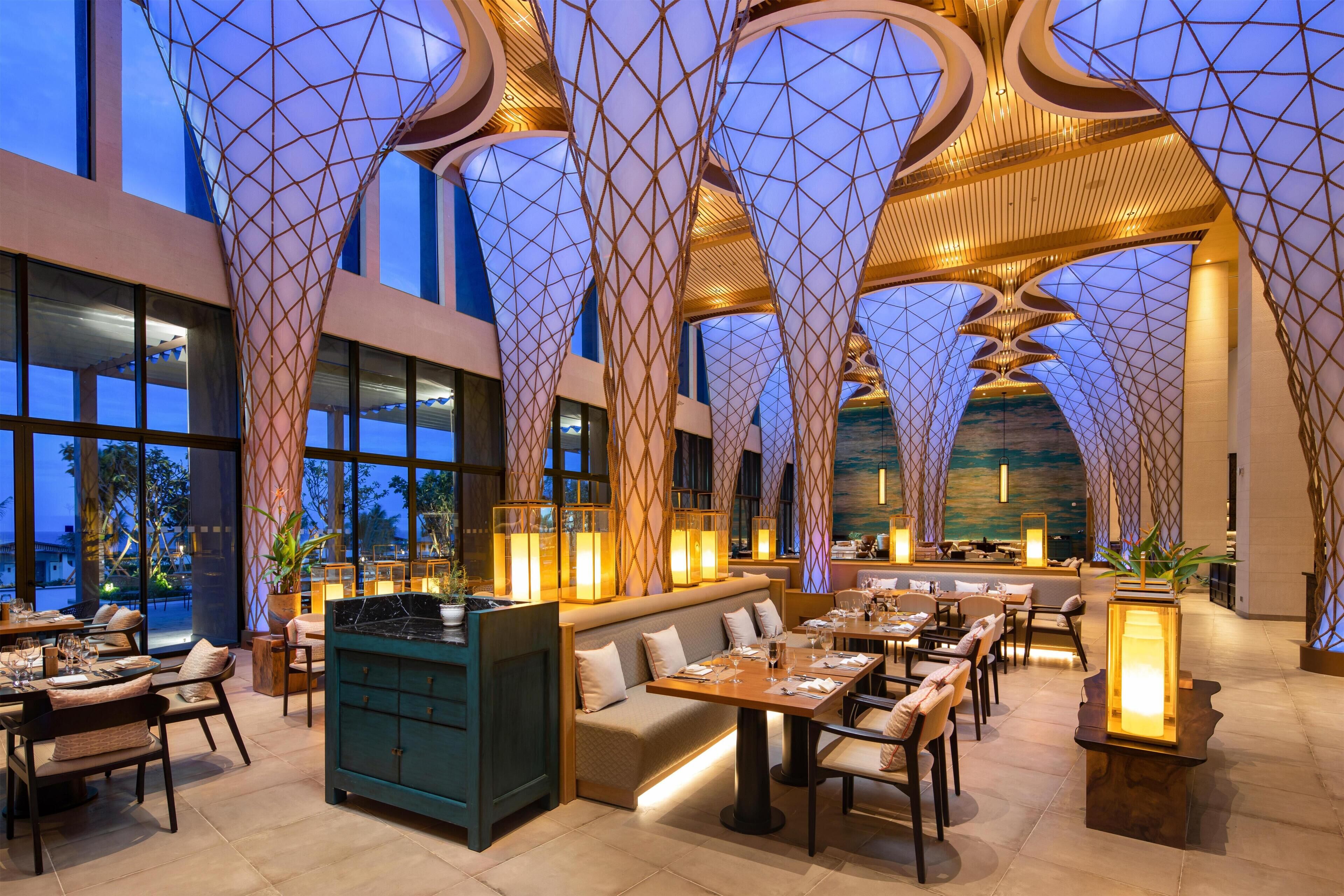 A spacious restaurant with high ceilings, large windows, and modern geometric lighting.
