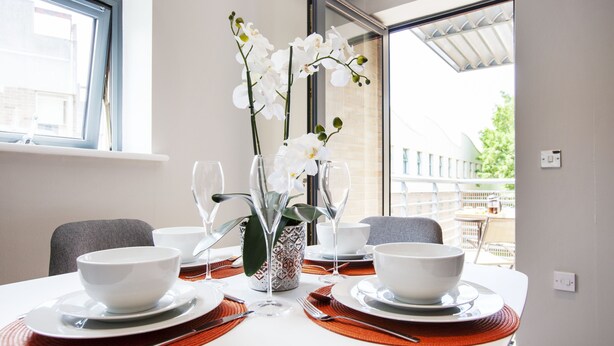 A dining table set with white bowls, plates, and cutlery, accompanied by a vase of white orchids and a patterned vase. - The Wesley Luxury City Apartment (Oxford)