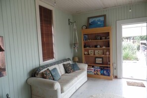 Uma sala de estar aconchegante com um sofá de cor clara, uma estante de madeira e uma janela com persianas.