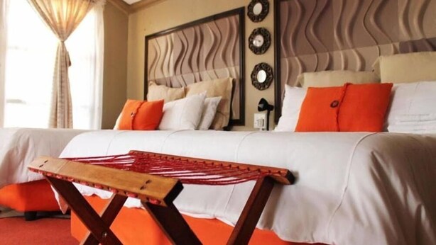 A hotel room with a large bed, a wooden headboard, and a view of the outdoors through a window with curtains.