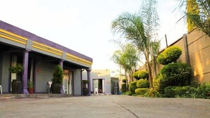 A building with a purple and yellow facade, a paved courtyard, and neatly trimmed bushes and trees.