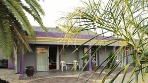 A building with a purple exterior, a covered patio with a patterned floor, and a palm tree in the foreground.