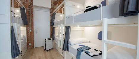 A dormitory room with bunk beds, a suitcase, and a brick wall.