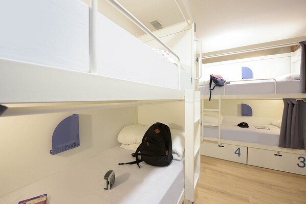 A bunk bed room with a blue sign on the wall, a black backpack on the lower bunk, and a white mattress on the upper bunk. -  Room Gran Vía (Madrid)