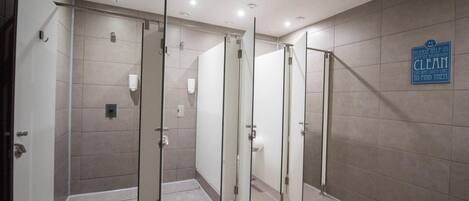 A modern restroom with glass partitions, a sign encouraging cleanliness, and a tiled floor.