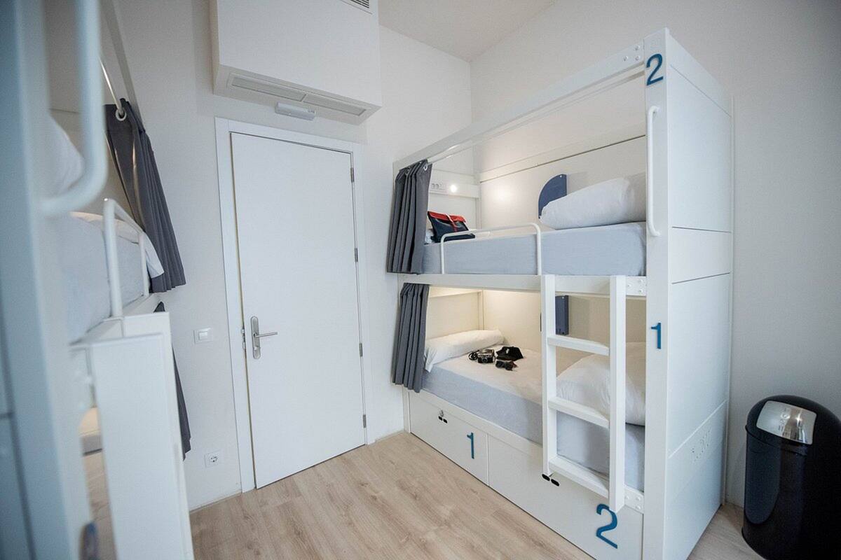 A compact room with bunk beds, a door, a small closet, and a trash bin.