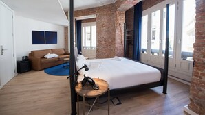 A modern hotel room with a large bed, a brick accent wall, and a view through large windows. -  Room Gran Vía (Madrid)