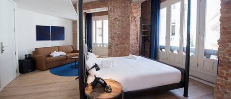 Une chambre d’hôtel moderne avec un grand lit, un mur décoratif en briques et une vue dégagée sur l’extérieur grâce à de grandes fenêtres.