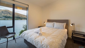 Un dormitorio moderno con una cama grande, una silla, una mesita de noche y vistas a un lago.