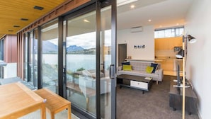 Una sala de estar moderna con un muro de vidrio que da a un lago, un sofá con cojines, una mesa de centro y un escritorio con una lámpara.
