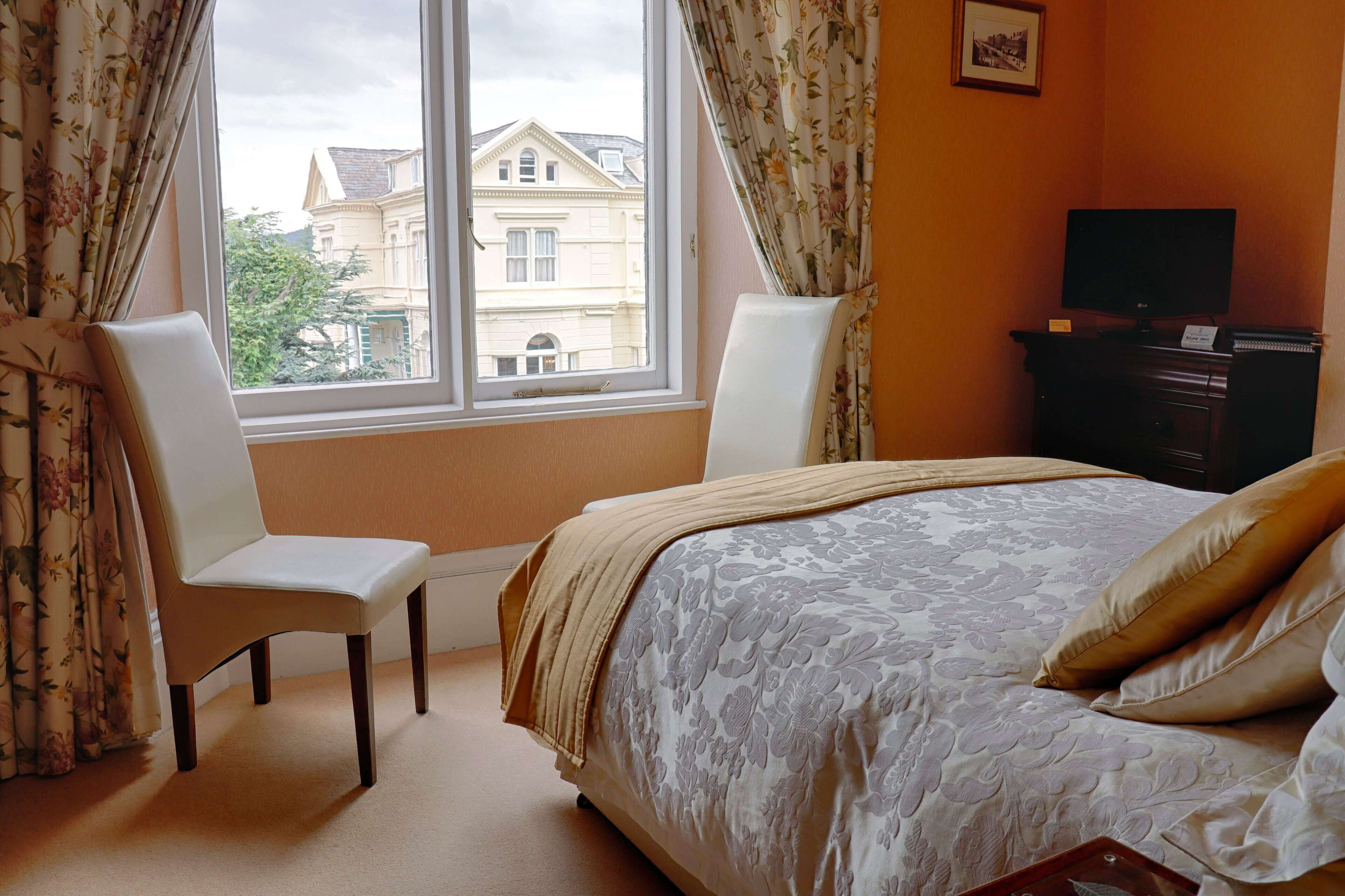 A bedroom with a bed, two chairs, a dresser, and a television.