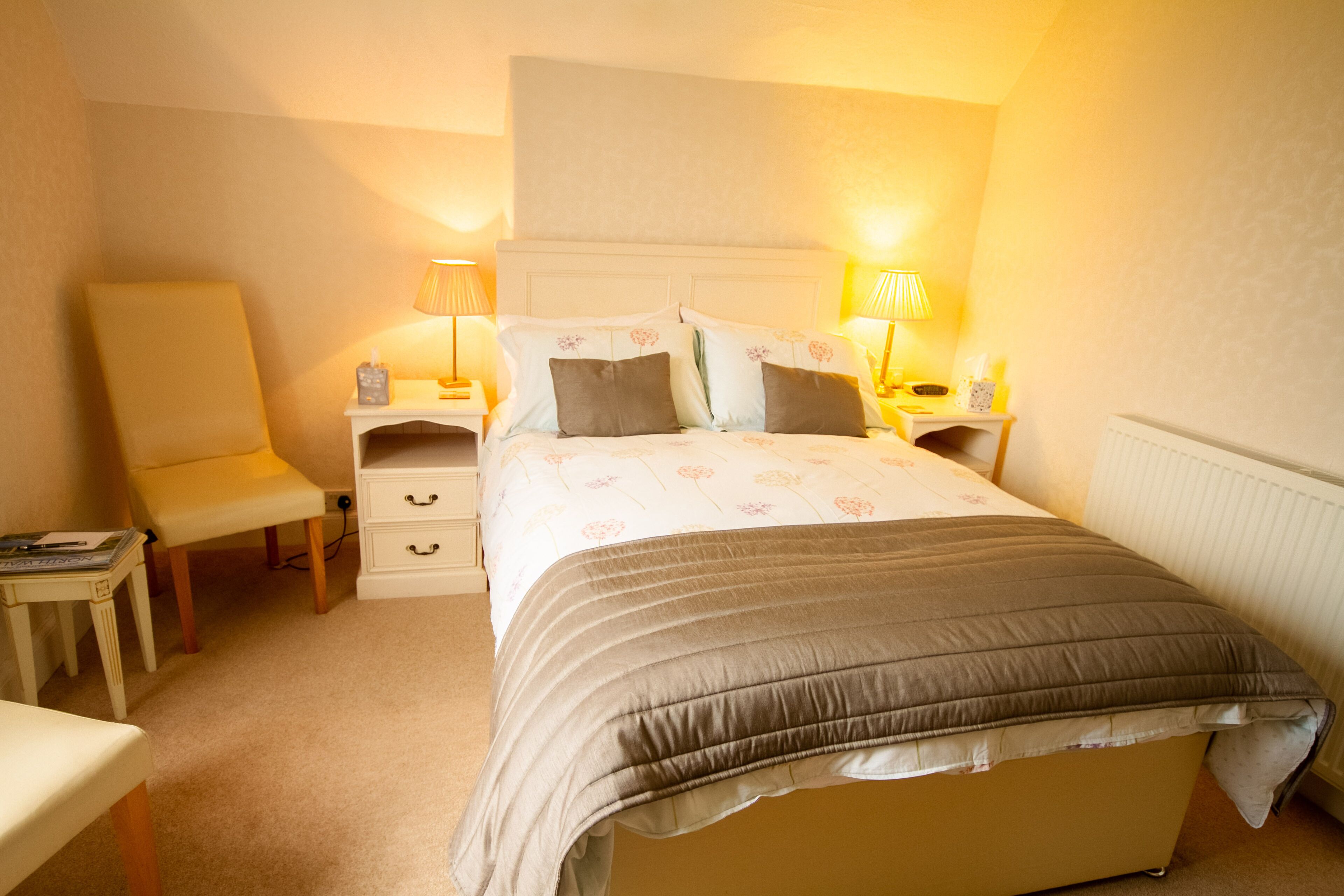 A neatly arranged bedroom with a bed, bedside tables, a chair, and a lamp.