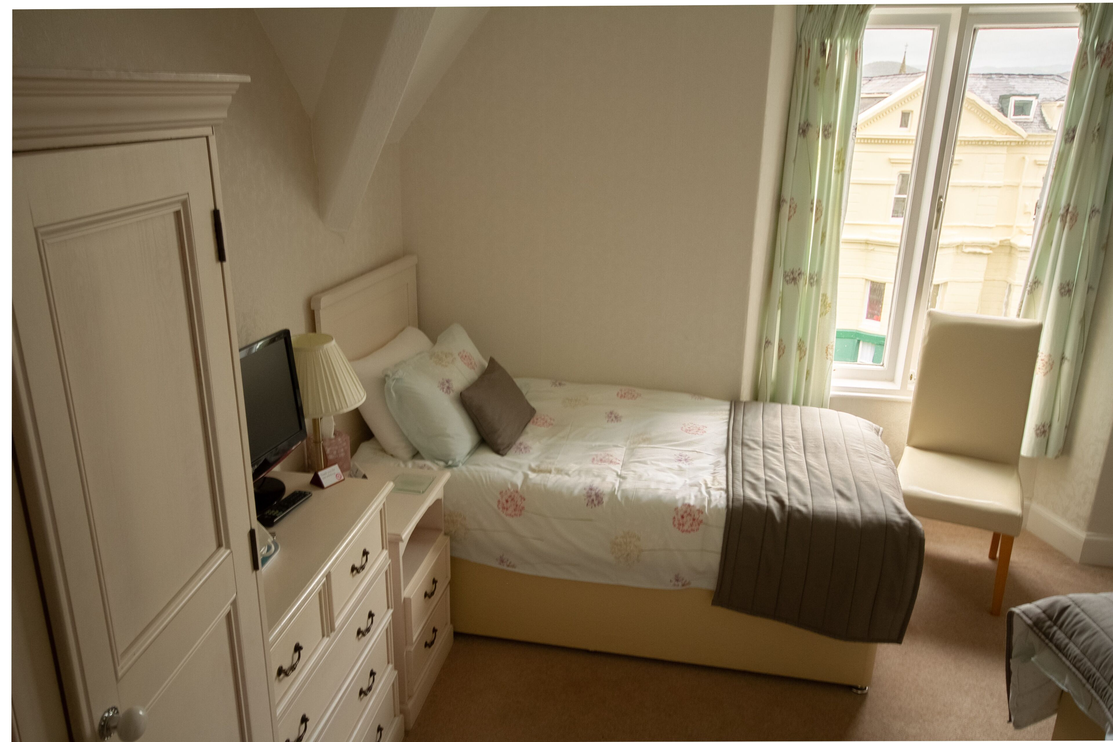 A bedroom with a bed, a dresser, a chair, and a window with curtains.