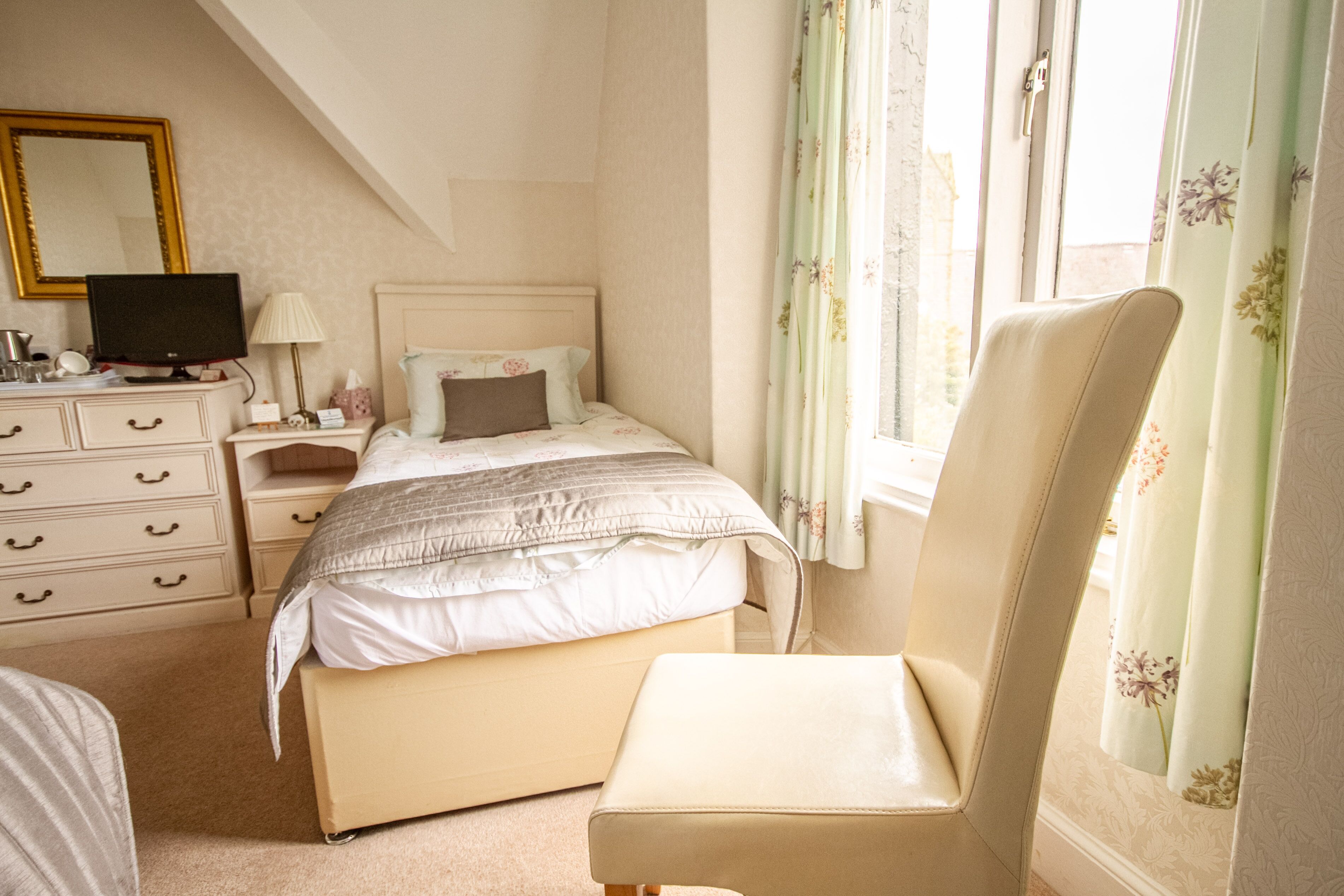 A bedroom with a bed, a chair, a dresser, a television, and a window with curtains.