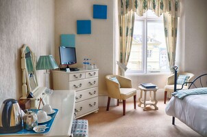 A hotel room with a bed, a desk with a computer, a chair, a dresser, a mirror, and a window with curtains.
