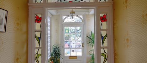 A hallway with a white door, stained glass windows, and potted plants.