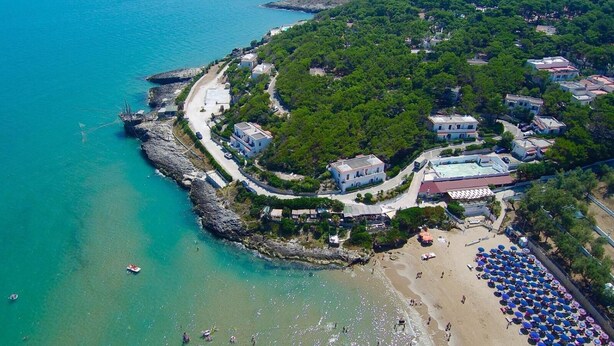Vista aérea de una zona costera con playa, costa rocosa y edificios rodeados de vegetación.