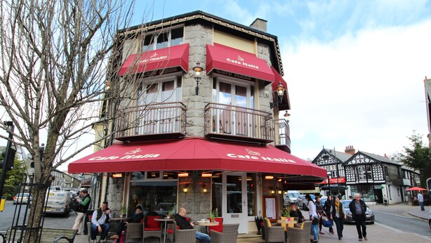 Un edifici de diversos pisos amb una cafeteria anomenada Cafe Italia a la planta baixa, que disposa d'una terrassa i façana de pedra.