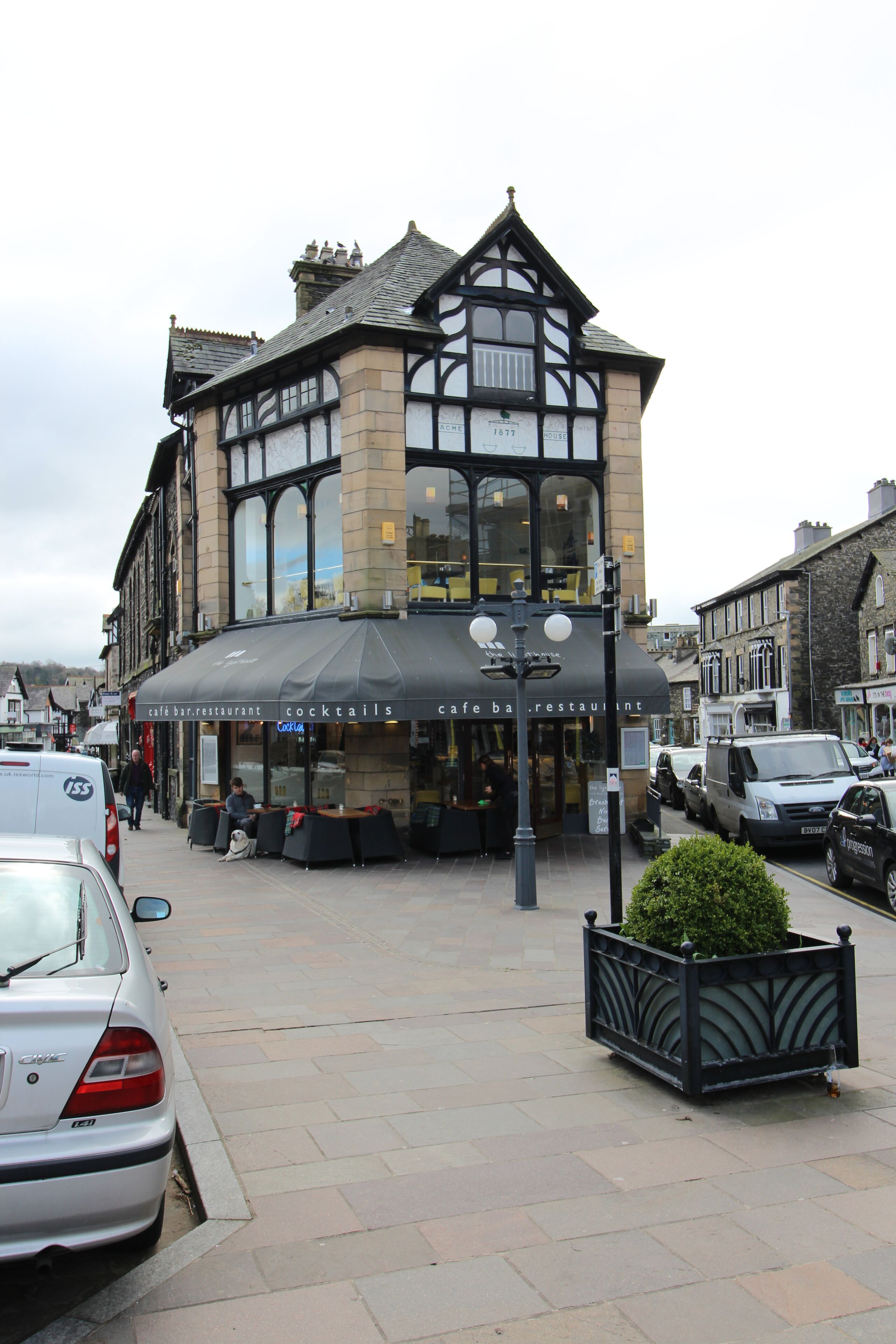 A traditional building with a cafe bar and restaurant on the ground floor, featuring large windows and a black awning.